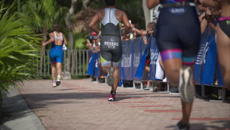A-group-of-four-athletes-running-passing-by-a-crowd-of-spectators-cheering-the-participants-at-a-triathlon-competition