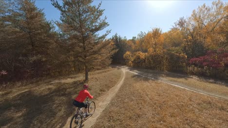 FPV-drone-following-mountain-biker-biking-on-a-dirt-path-during-autumn-season