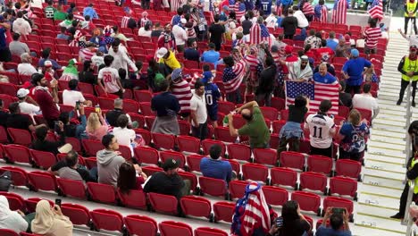 USA-Fans-in-the-stadium-al-thumama-are-support-their-football-player-team-with-the-USA-flag-in-the-red-seats-near-the-pitch-green-field-of-the-stadium-with-beautiful-architectural-design-with-friends