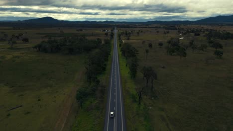 Modern-silver-car-driving-on-highway-along-a-lush-green-gum-tree-forest-and-mountains