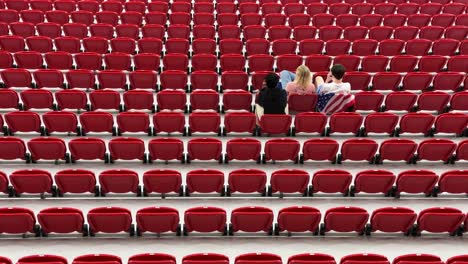 A-couple-sit-in-the-red-seats-of-stadium-hopeful-and-excited-to-watch-the-football-match-between-USA-Iran-in-Doha-Qatar-makes-red-pattern-shapes-focused-perspective-wide-view-landscape-interior-design