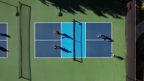 Two-teams-playing-Pickleball-outside,-birds-eye-aerial-view-from-above-on-blue-clay-court