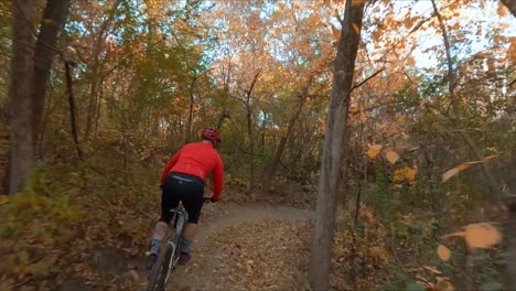 FPV-drone,-man-mountain-biking-on-a-dirt-road-in-the-forest-during-autumn-season