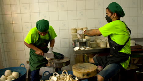 Thailand,-Bangkok---13-August-2022:-Two-men-working-industry-backroom-cutting-top-of-fresh-green-coconut-peeled-pouring-coconut-water-into-pot