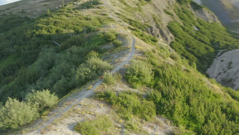 Two-mountainbikers-walking-uphill-on-gravel-path-ridge-in-mountains,-aerial