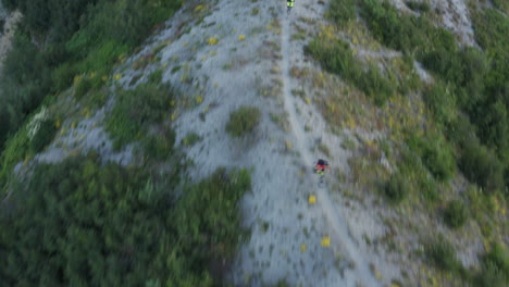 Extreme-downhill-mountainbiking-going-down-gravel-trail-on-mountain-ridge,-aerial