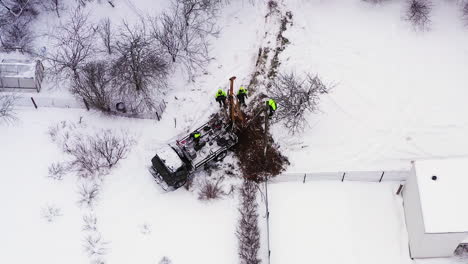 Aerial-view-above-engineer-workers-replacing-damaged-electricity-pole-on-snow-covered-rural-farmland