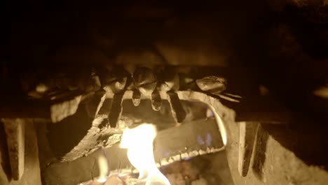Flames-gently-burn-two-logs-in-a-fireplace-covered-by-an-old-grate-in-a-remote-bothy-in-Scotland