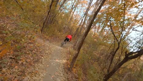 FPV-drone-following-mountain-biker-through-forest-dirt-path-during-autumn-season