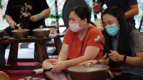 Zwei-Asiatische-Frauen,-Die-Während-Einer-Live-performance-Ein-Gesicht-Schlagendes-Südostasiatisches-Bonang-schlaginstrument-Tragen,-Gefilmt-Als-Mittlere-Aufnahme-Im-Handheld-stil