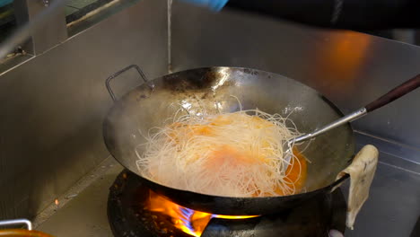 Thailand,-Bangkok---18-August-2022:-Cooking-dry-noodles-in-hot-sauce-of-pad-thai,-adding-veggies-into-hot-pan-wok-in-restaurant