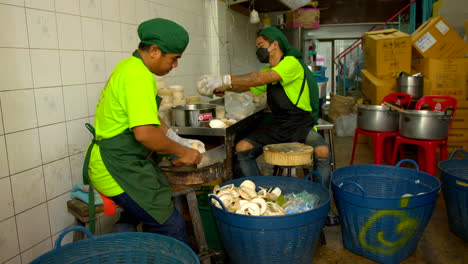 Thailand,-Bangkok---13-August-2022:-Two-men-worker-cutting-peeled-coconut-using-cleaver-preparing-bowl-for-coco-jelly
