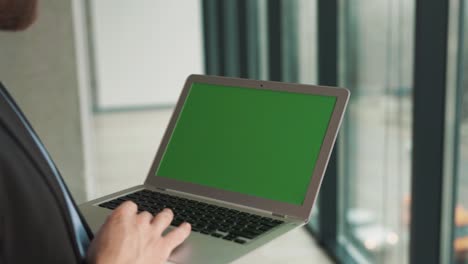 Close-up-of-a-laptop-screen-with-a-chromakey-in-the-hands-of-a-man-on-the-background-of-a-panoramic-window