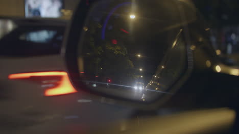 Close-up-of-car-mirror-in-European-city,-reflecting-street-traffic,-night