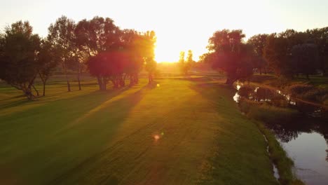 Smoove-aerial-drone-shot,-low-angle-above-the-ground-on-the-golf-course-during-a-sunny-amazing-sunset
