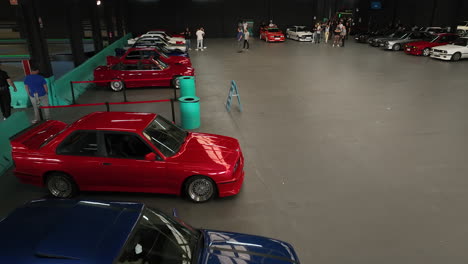 Indoor-aerial-of-BMW-e30-car-meeting,-many-vintage-colorful-vehicles,-dolly-in