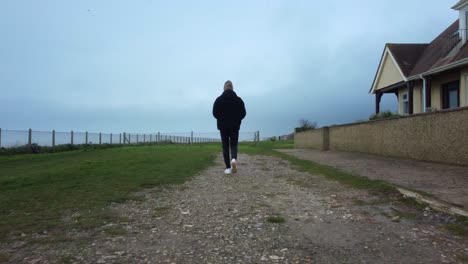 Following-man-walking-along-clifftop-coastal-path-in-overcast-weather