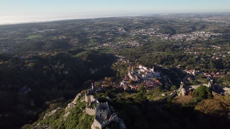 Cinematic-drone-shot-flying-above-ruins-of-Castelo-dos-Mouros-and-slowly-revealing-old-town-of-Sintra-and-vastness-of-landscape,-Lisbon,-Portugal