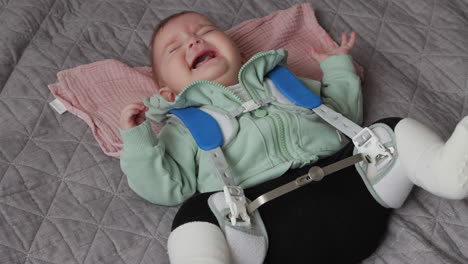 Baby-girl-in-Pavlik-Harness-to-correct-Hip-Dysplasia-cries-while-lying-on-back