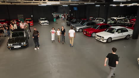 Aerial-view-following-BMW-e30-club-fan-admiring-classic-vehicles-parked-in-warehouse-car-show-meeting
