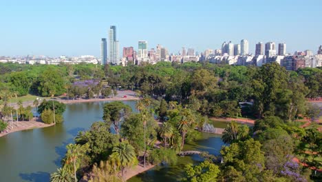 Aerial-view-establishing-the-lake-of-the-rose-garden-of-Palermo-with-the-residential-buildings-of-Buenos-Aires-in-the-background,-Argentina