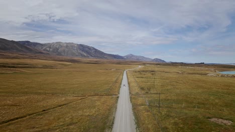 A-vehicle-navigating-a-rough,-dirt-path-surrounded-by-barren,-rural-landscapes-with-majestic-mountains-and-a-tranquil-lake-in-the-distance,-bathed-in-warm-sunlight