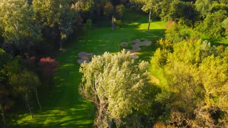 High-angle-establishing-drone-shot-flying-close-trees-above-golf-course,-revealing-sand-bunkers-and-a-golf-hole-during-sunny,-summer-day-in-Warsaw,-Poland