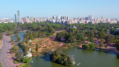 Aerial-view-dolly-in-the-lake-of-the-Palermo-Rose-Garden-on-a-sunny-day,-residential-buildings-of-the-city-of-Buenos-Aires-in-the-background,-Greek-bridge