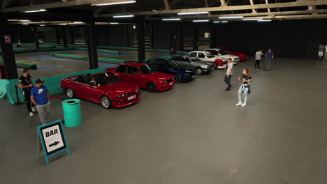 Various-old-school-BMW-e30-vehicles-parked-in-warehouse-club-meeting,-orbiting-aerial-view