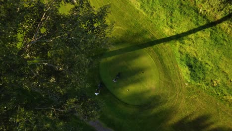 Drone-aerial-footage-4K-with-golfers-walking-on-the-putting-green-during-a-sunny-day-on-golf-course-practice