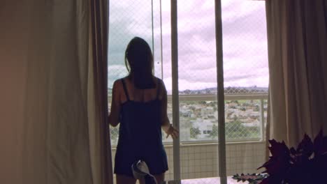 Silhouette-of-brunette-woman-opening-home-balcony-sliding-doors-in-slow-motion-on-a-windy-overcast-day