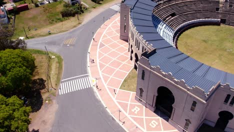 Aerial-view-of-a-couple-of-friends-walking-around-the-Real-de-San-Carlos-bullring-in-Colonia-del-Sacramento,-Uruguay-on-a-sunny-day