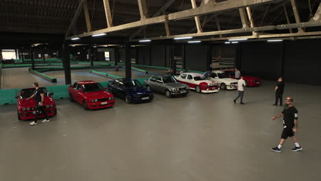 Old-school-underground-BMW-e30-club-meeting-event-in-go-kart-warehouse,-aerial-view-dolly-right