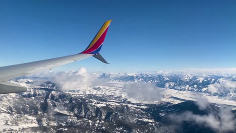 Southwest-Plane-Wing-Flying-Above-Rocky-Mountain-Range-Winter