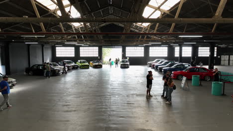 Indoor-show-with-BMW-e30,-vintage-cars-in-bright-colors,-aerial-shot,-many-fans
