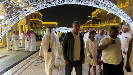 Menschen-Mit-Arabischen-Kleidern-Für-Männer-Und-Frauen-Gehen-In-Einer-Luxusstraße-In-Katara,-Katar,-Doha,-Antike-Architektur,-Kleine-Kette-Aus-Led-licht,-Fußballdekoration,-Struktur-Und-Schmuckeinkaufszentrum