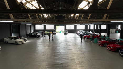 Descending-aerial-view-from-warehouse-roofing-to-classic-BMW-e30-club-car-show-exhibition