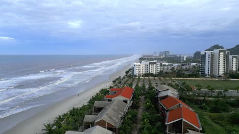 Stunning-flyover-of-An-Bang-Beach-in-Vietnam-while-waves-are-hitting-the-sandy-beach-and-lush-greenery