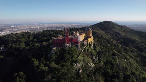 Drone-flying-close-to-historic-Pena-Palace-castle-standing-a-top-of-a-hill-in-Sintra-mountains-above-town-of-Sintra,-Portugal
