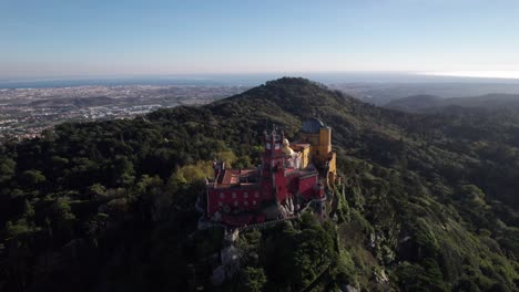 Cinematic-drone-shot-circling-around-historic-Pena-Palace-castle-standing-a-top-of-a-hill-in-Sintra-mountains-above-town-of-Sintra,-Portugal