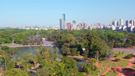 Dolly-in-aerial-view-of-the-contrast-between-the-Palermo-Rose-Garden-and-the-new-residential-buildings-of-Buenos-Aires-in-the-background,-sunny-spring-day