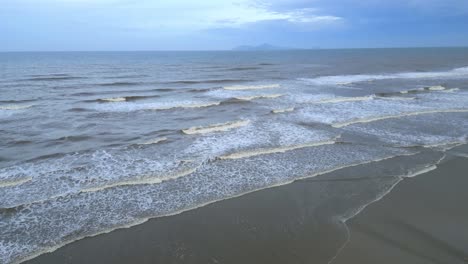 Stunning-slowmotion-aerial-tilt-shot-of-the-ocean-white-waves-hitting-the-sandy-beach
