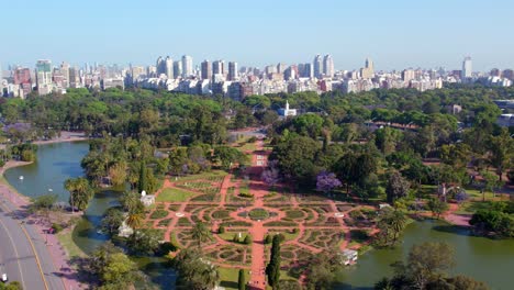 Aerial-view-dolly-in-the-design-of-the-palermo-rose-garden-with-the-skyline-of-the-neighborhood-in-the-background,-residential-buildings-of-the-city-of-Buenos-Aires,-Argentina