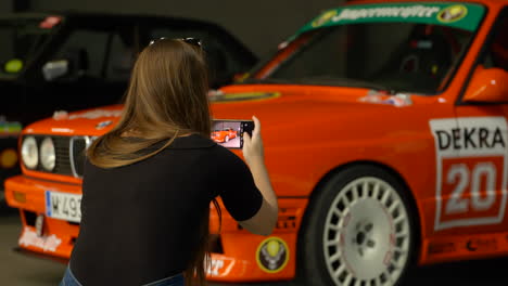 Woman-takes-photos-of-BMW-e30-cars-at-indoor-fan-meeting-exhibition,-close-up