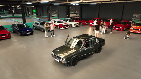 Classic-shiny-green-BMW-e30-arriving-at-club-warehouse-car-show-event,-Orbiting-aerial-view