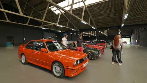 Low-gimbal-shot-circling-around-orange-BMW-e30-with-people-looking-around