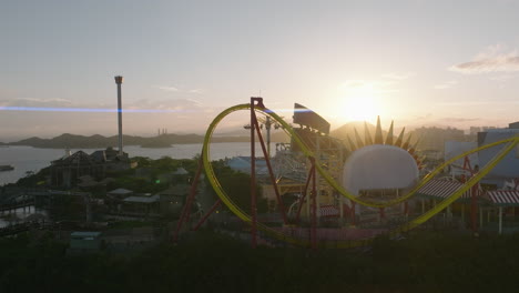 Approaching-shot-of-'Hair-Raiser'-rollercoaster-and-'Whirly-Bird'-attraction-in-Ocean-Park,-Hong-Kong-during-sunset-with-anamorphic-sun-flares