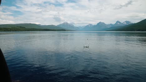 Girl-skipping-rock-in-slow-motion-on-glacial-lake-at-Glacier-National-Park-with-mountain-range-backdrop