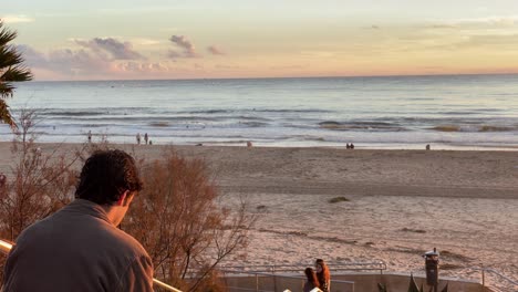 Silhouette-Eines-Mannes,-Der-Eine-Zigarette-Raucht-Und-Bei-Sonnenuntergang-Mit-Ozean-Im-Hintergrund-über-Den-Strand-Nachdenkt