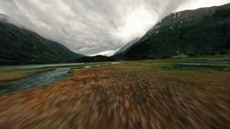 FPV-drone-flying-over-Alaskan-lake-with-storm-clouds-and-lush-green-mountain-range-in-the-background